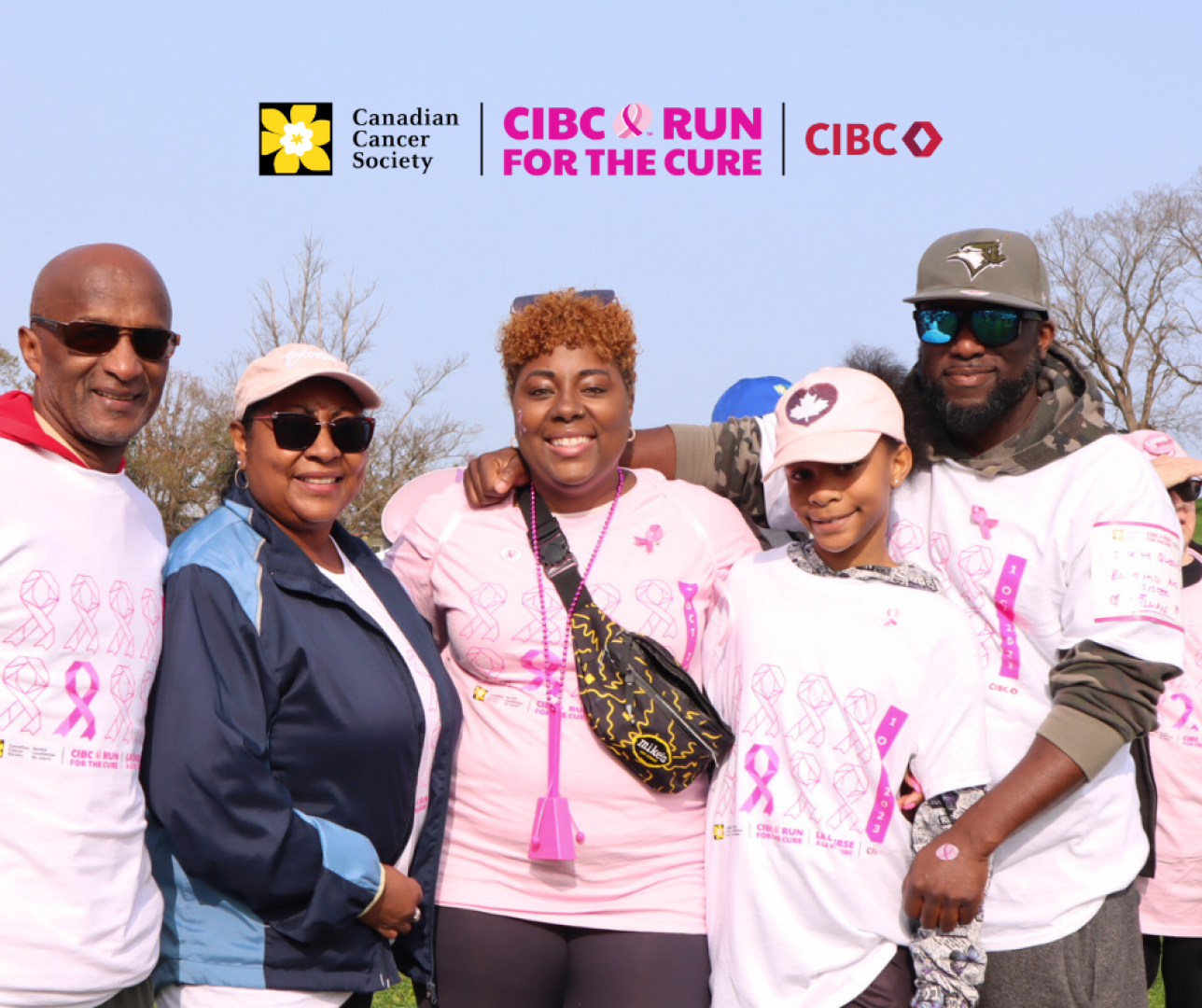 Four adults and one child, all wearing pink shirts, smile at the camera