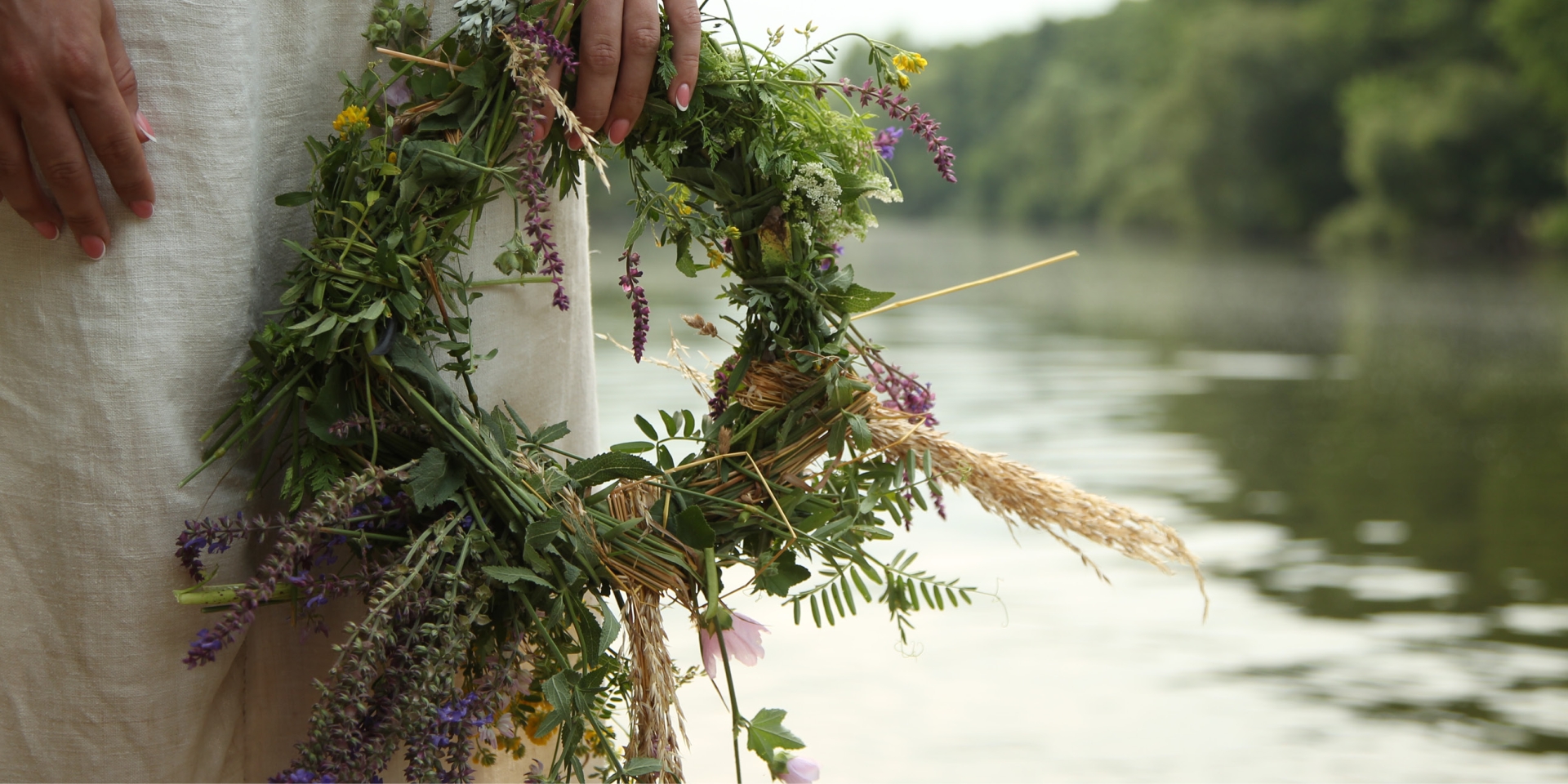 a woman holding a Ukrainian flower crown (vinok) in front of a river