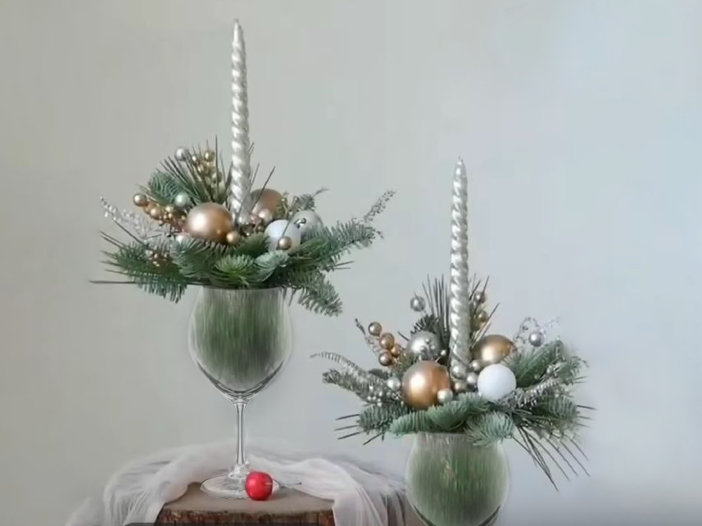 Two centerpieces made with a wine glass, fresh greenery, and festive ornaments.