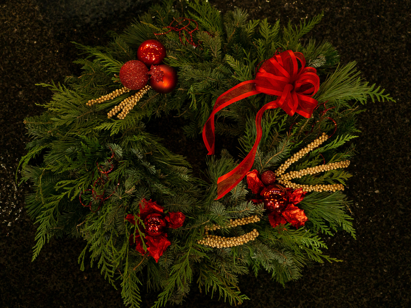 Traditional holiday wreath made from fresh greenery, red and gold festive ornaments.