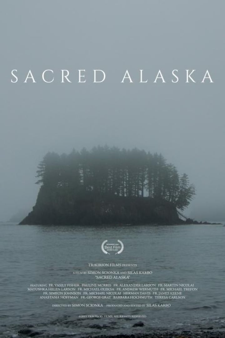 Image is of movie Sacred Alaska, with a small island covered in trees surrounded by water, in the fog. Entire image is grey toned. 