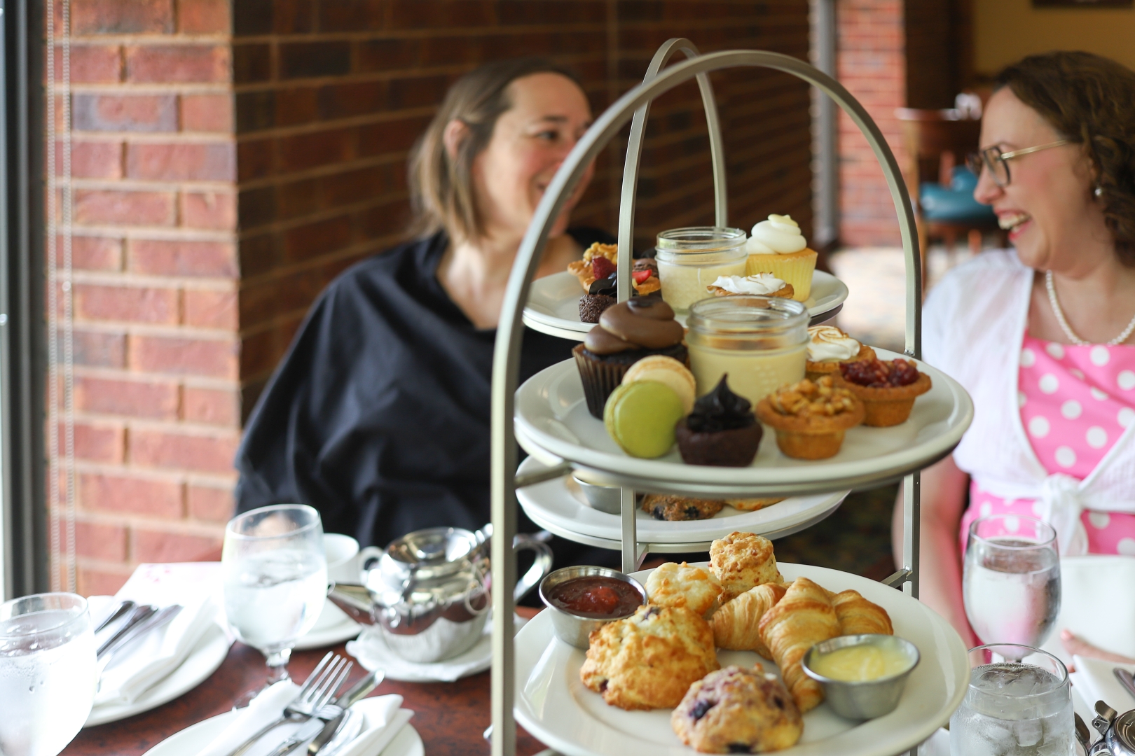 Two women laughing behind serving plates filled with pastries and desserts