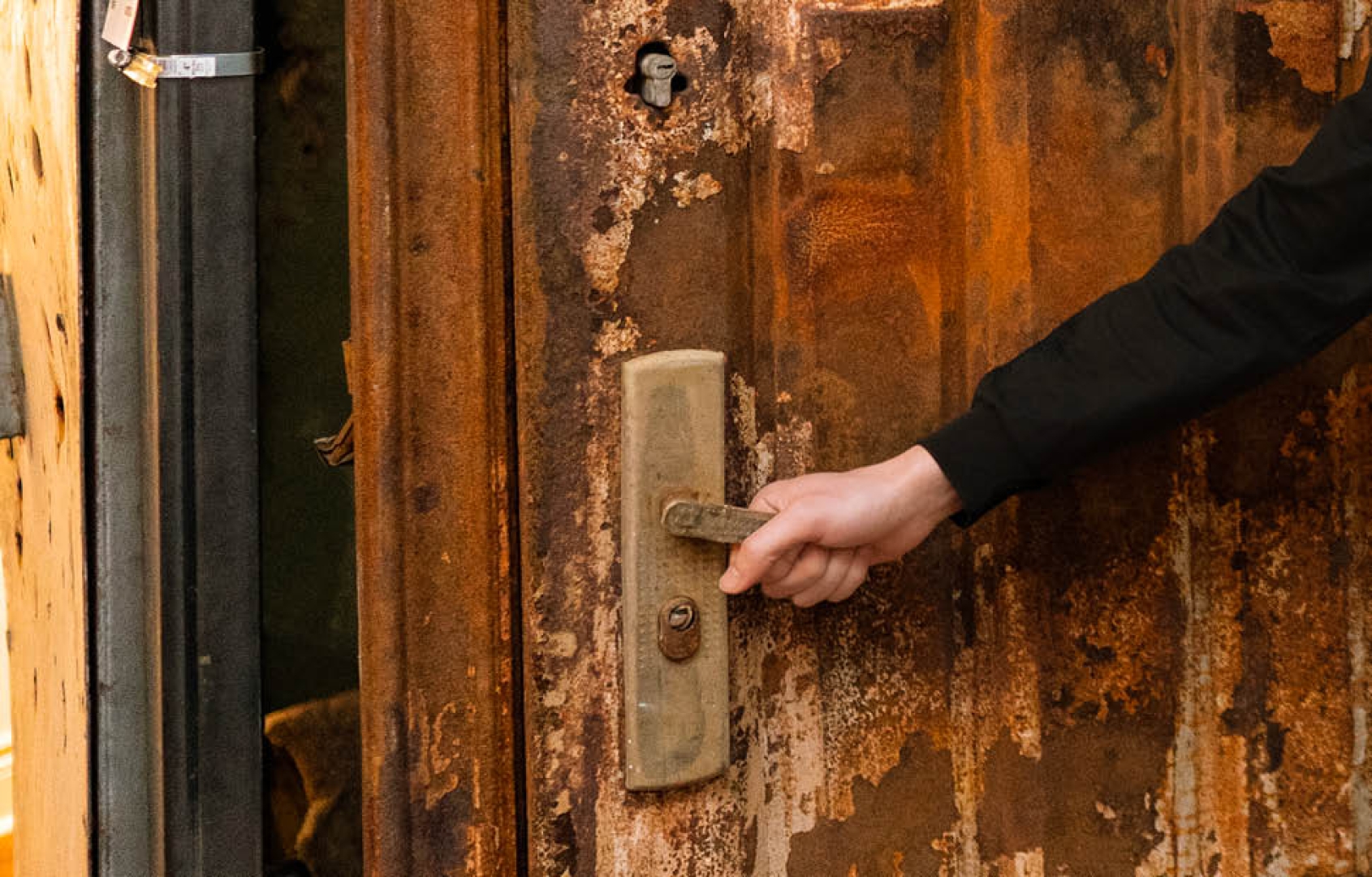 a hand turning a door handle and opening a damaged brown door