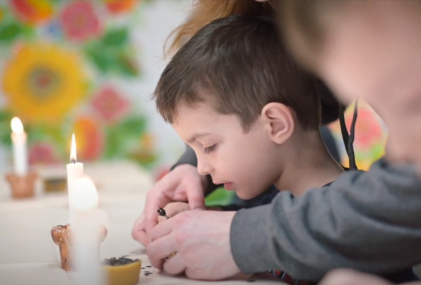 an adult helps a young child write with beeswax on a Ukrainian Easter egg (pysanka)