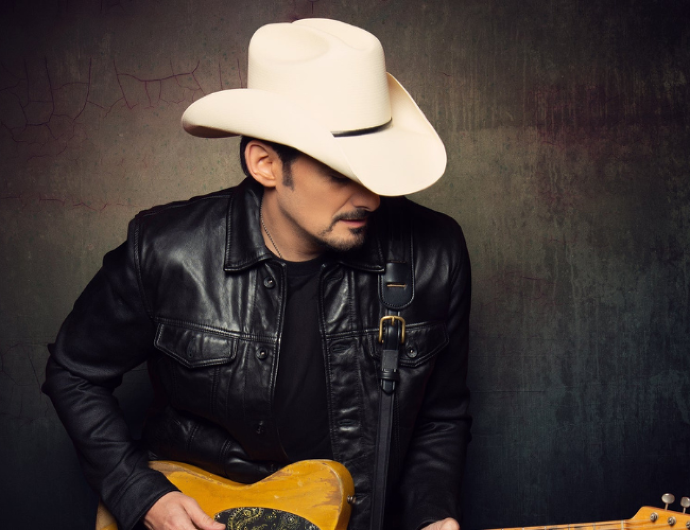 Man with a brimmed hat holding a guitar. 