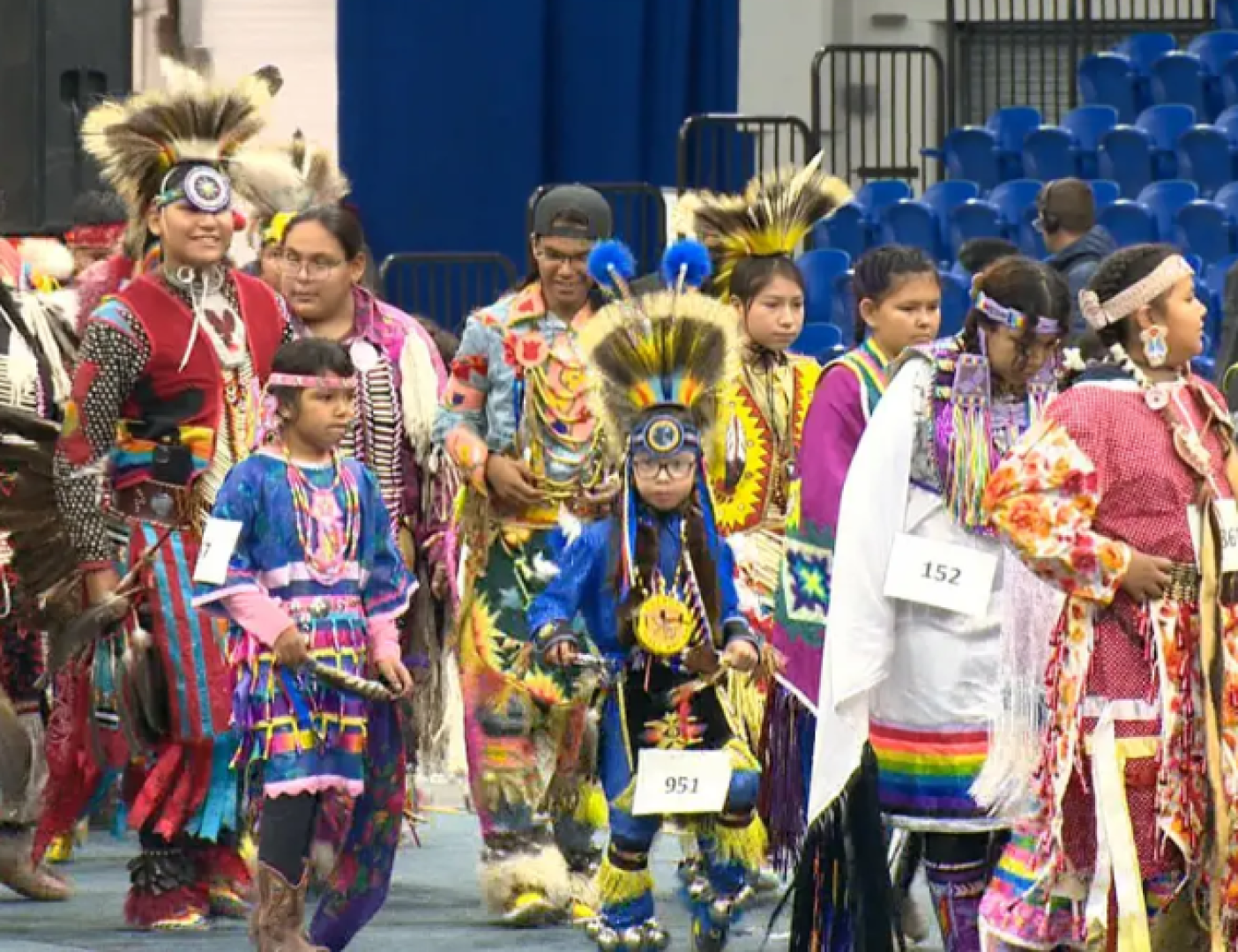 People in a line wearing Powwow regalia. 