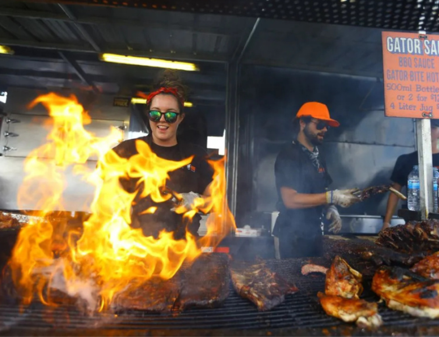 Person grilling beef with fire blazing.