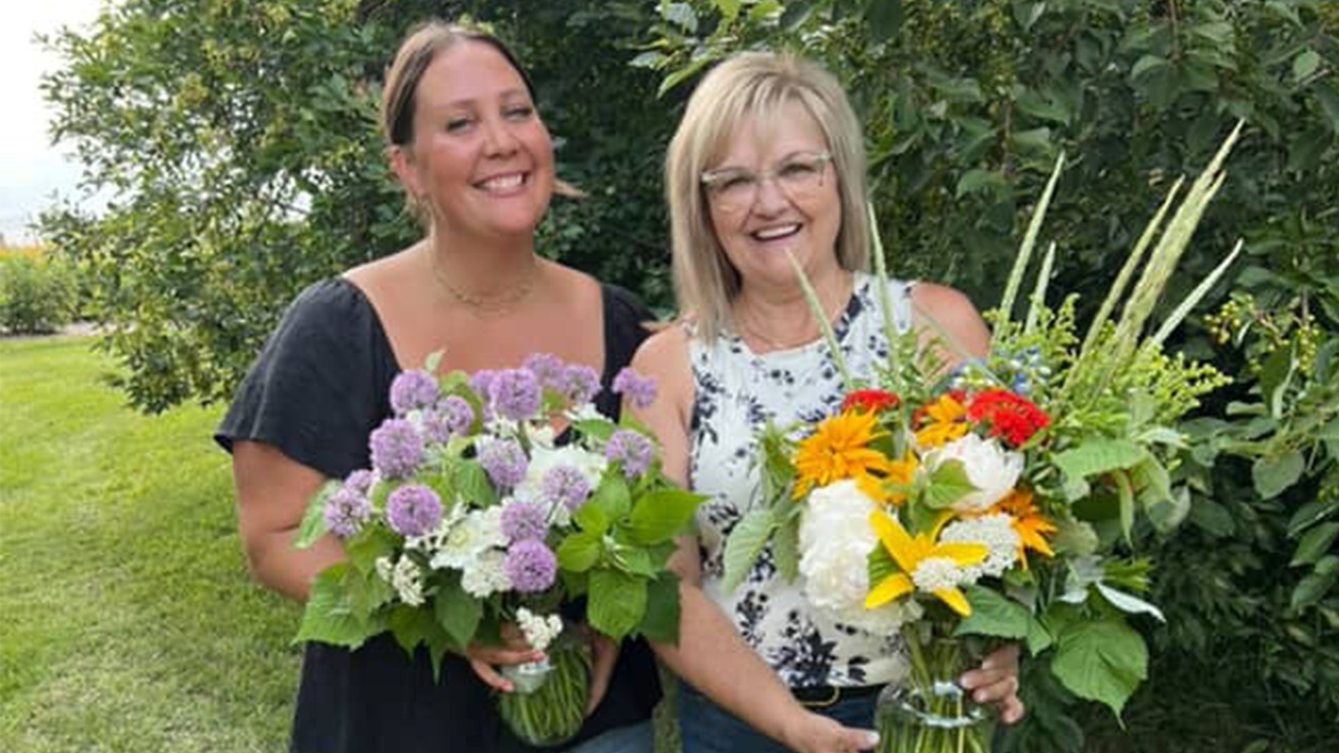 Two women stand outside at Black Fox Farm and Distillery holding flower arrangements after attending a flower class.