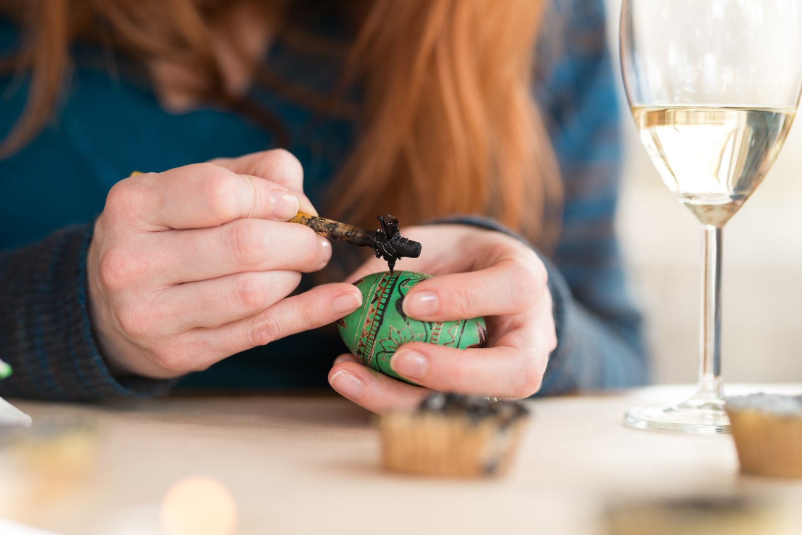 Close up of a woman writing pysanka with a glass of wine on the table
