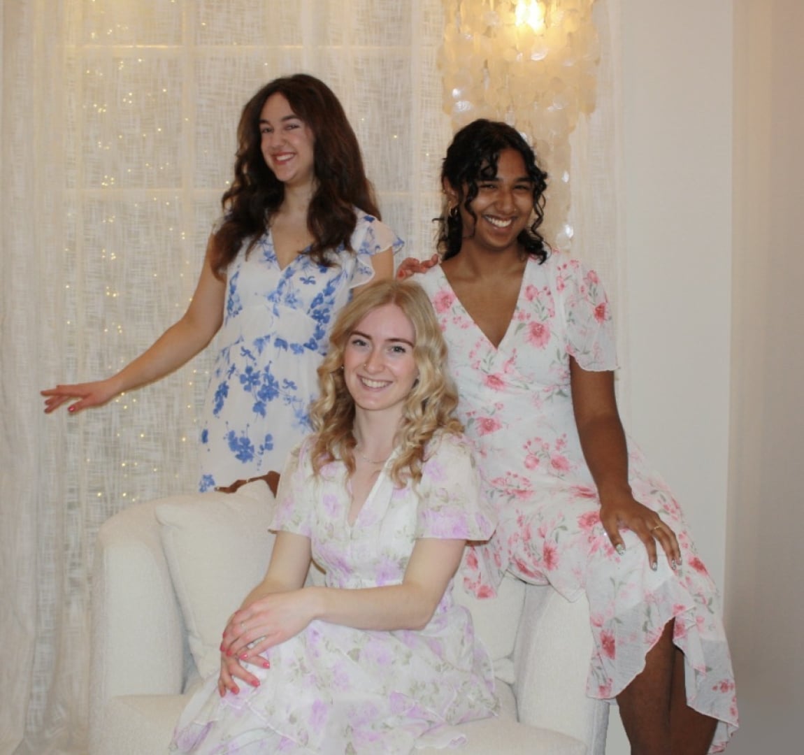 members of the petit-tones vocal trio Paulina Salisbury, Emma Gillingham and Sanjana Brijlall in floral dresses with a light shining behind.