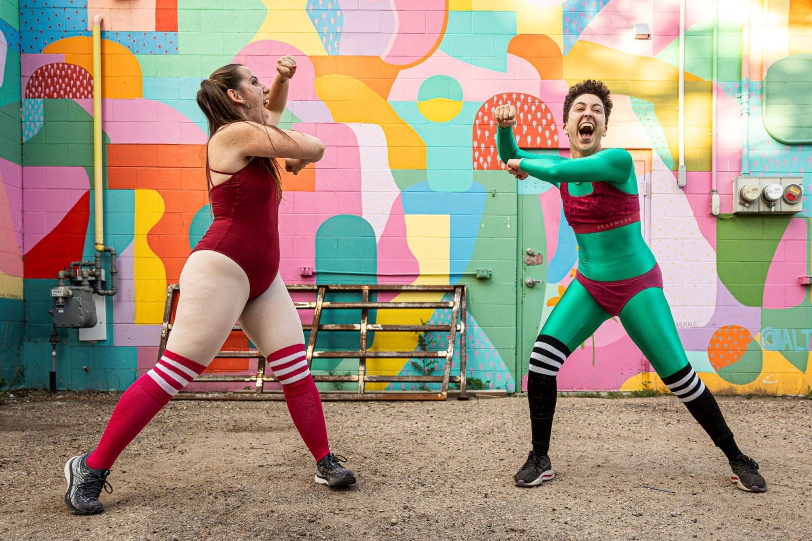 two dancers move excitedly in front of a colourful wall mural