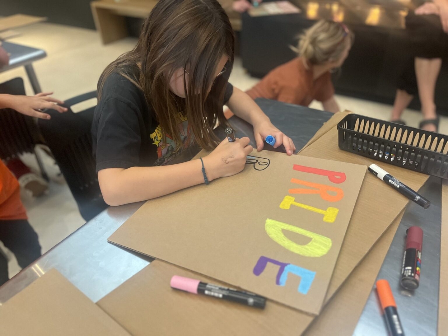 Youth participating in making pride signs using colourful markers on cardboard.