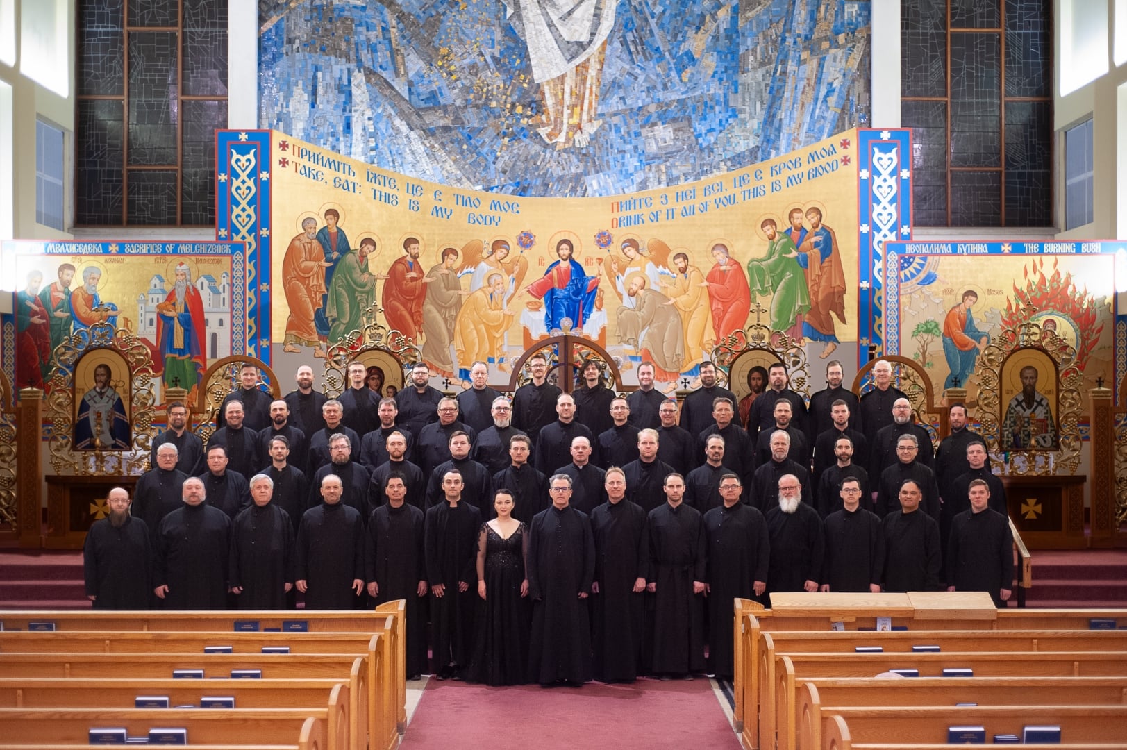 The Axios Men's Ensemble of over 50 performers in church, arranged in front of a Christian mural.