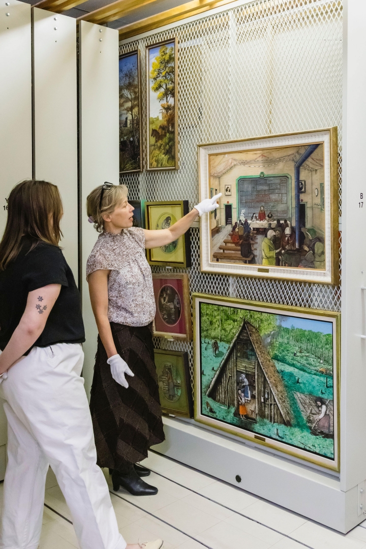 A photo of Dr. Jen Budney, Executive Director & CEO of the Ukrainina Museum of Canada, giving a tour of the collection and pointing to one of the Kurelek's paintings.