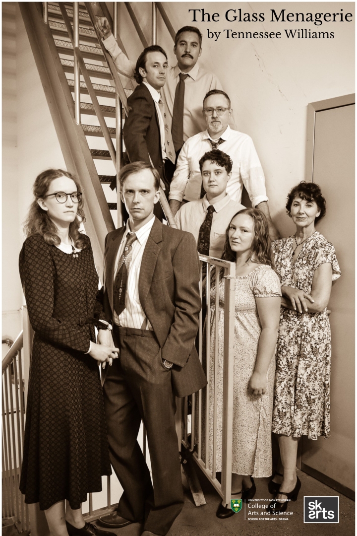 A group of actors in 1930s dress stand stoically against a steep metal staircase.