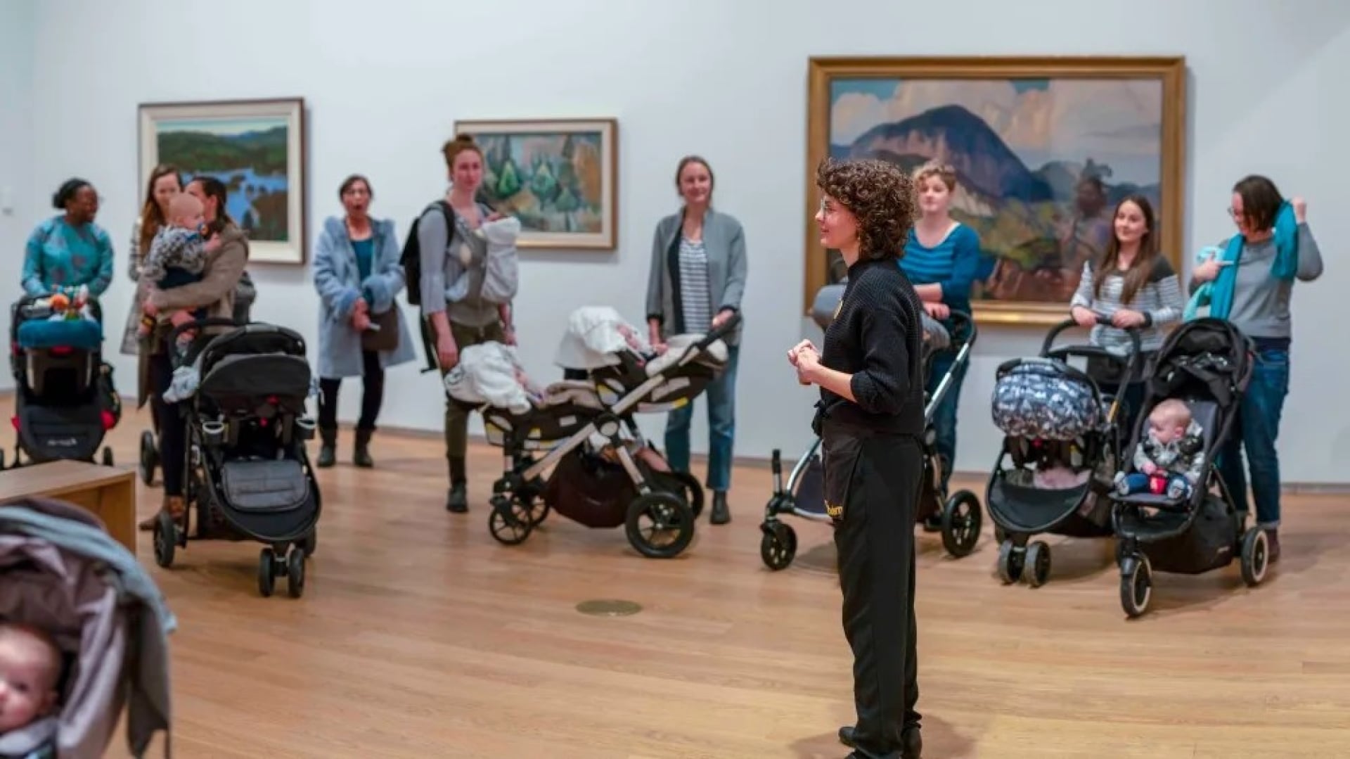 A group of caregivers and children, some in strollers, gather around a Remai Modern program guide for a tour.