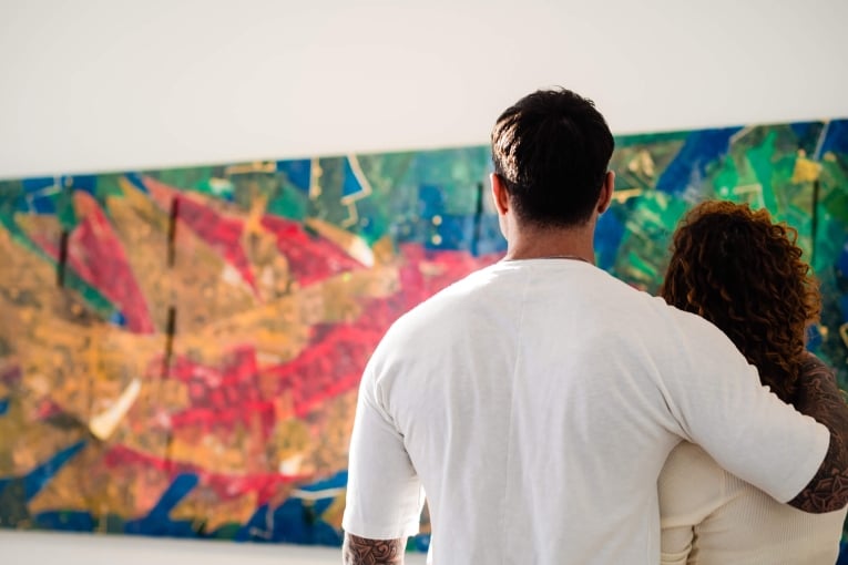 man with his arm around a woman looking at a large piece of artwork